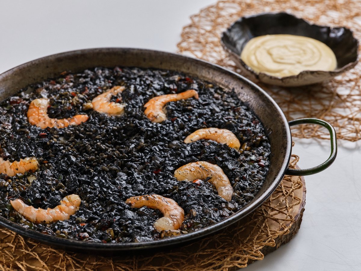 Arroz negro con camarones en una sartén sobre una mesa.