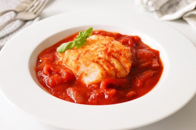 Un plato blanco con pescado en salsa de tomate.