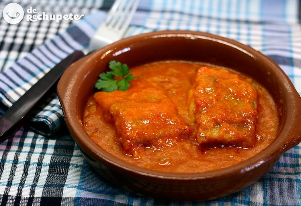 Un plato de pescado en salsa roja con un tenedor.